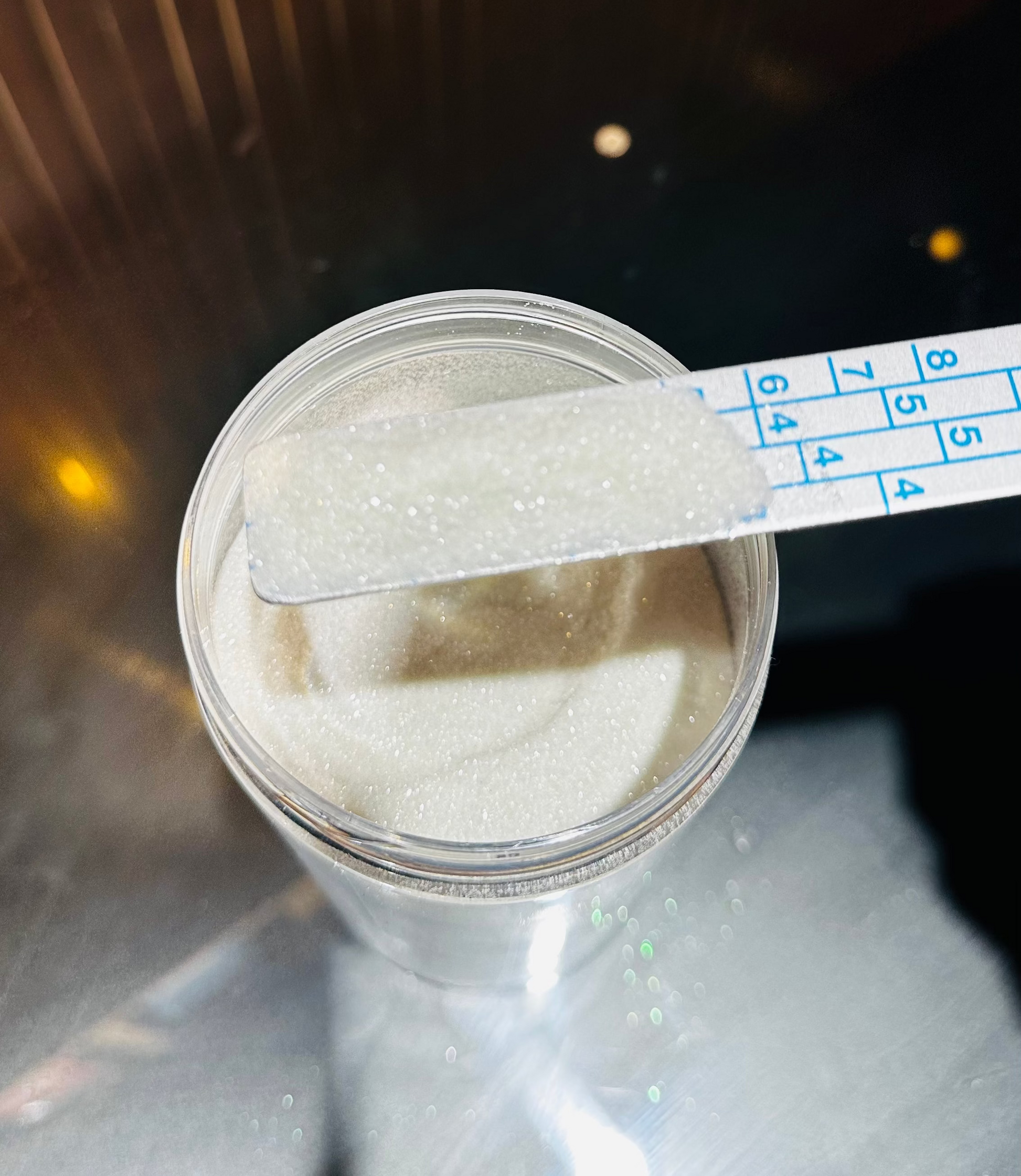 Clear container with white powder and a measuring spoon on a reflective surface