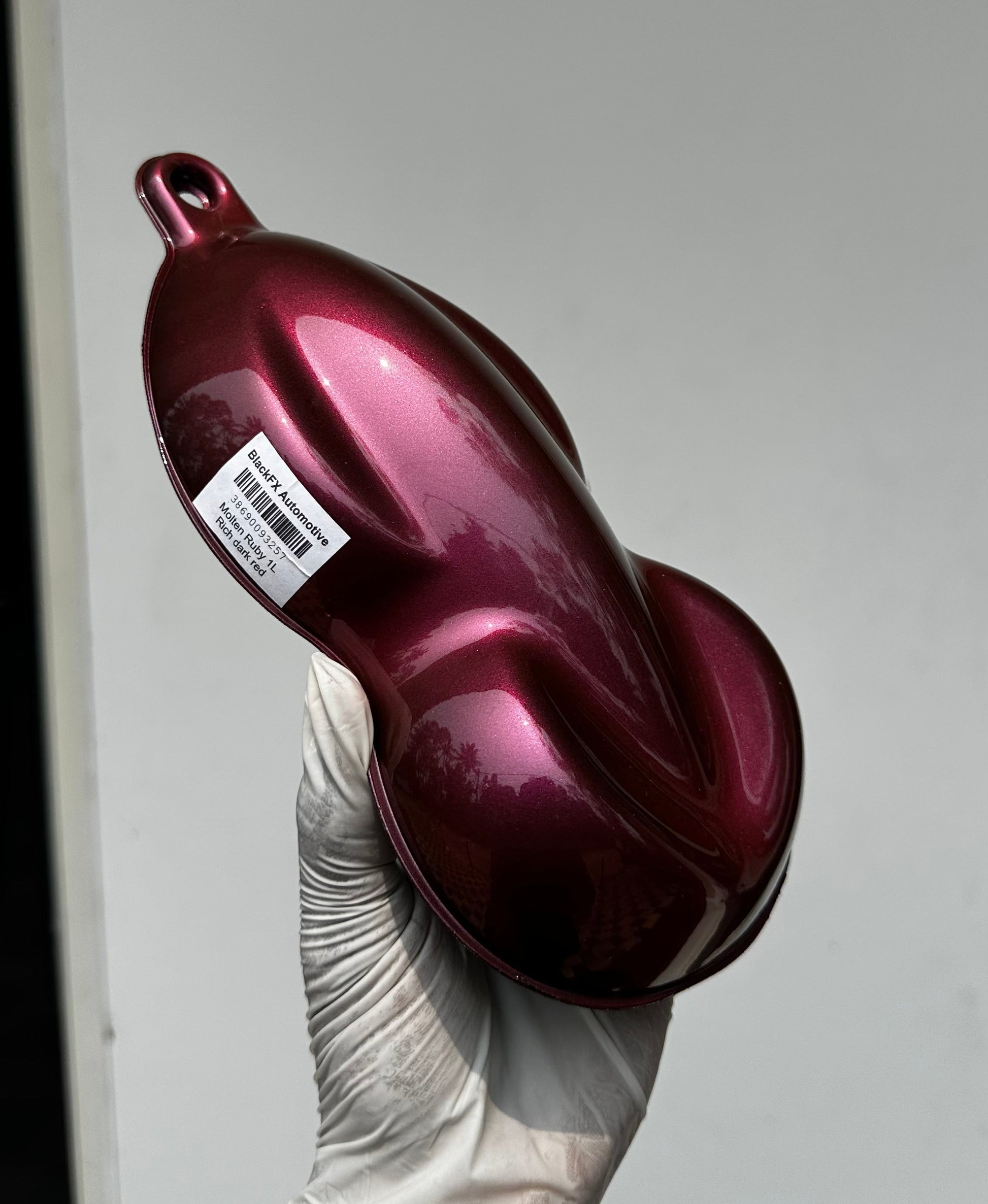 Maroon bottle with a label held by a gloved hand against a gray background